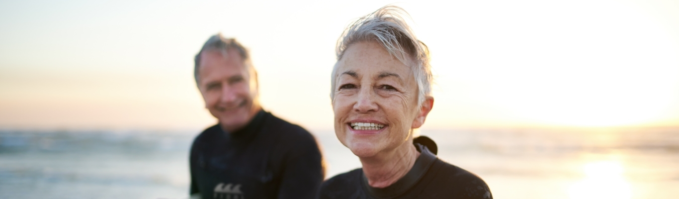 Senior couple walking along beach with surfboards