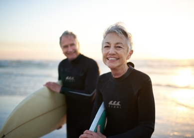 Senior couple walking along beach with surfboards 